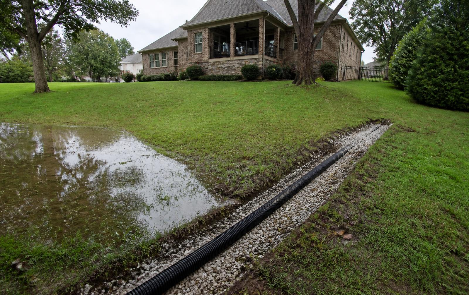 Standing water on a sloped Nashville-area backyard lawn beside a new gravel drainage trench with perforated pipe